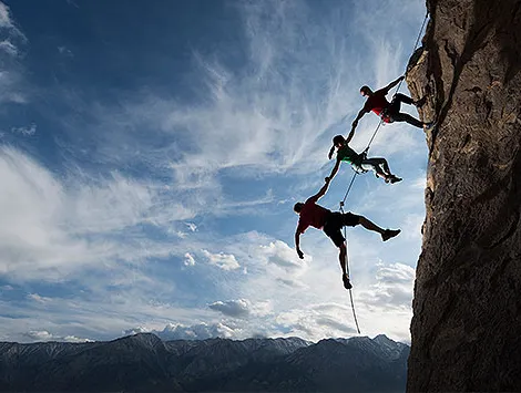 Three rock climbers helping one from falling in a dramatic setting