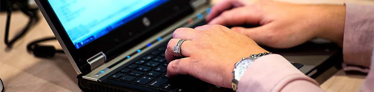 A man's hands wearing a watch and ring typing on a laptop keyboard.