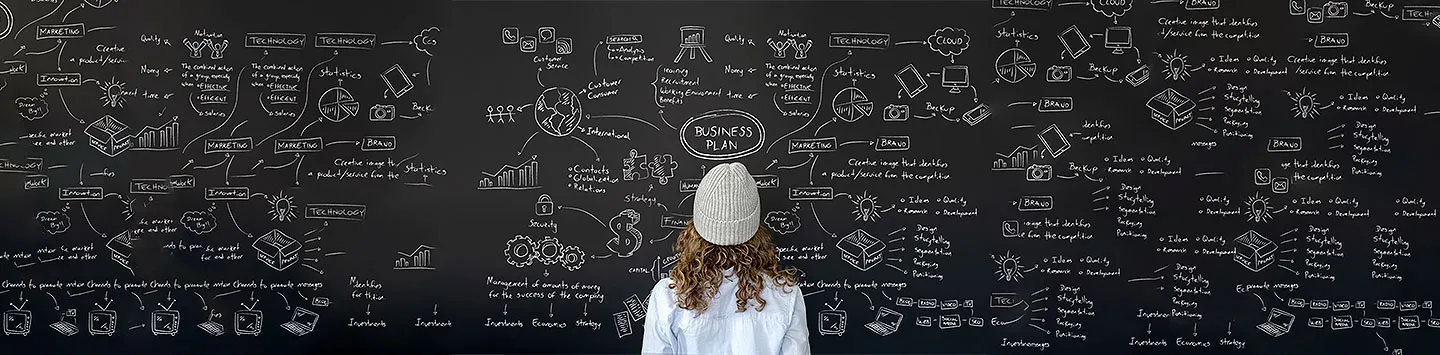 A female entrepreneur looks at a blackboard with a business plan outline on it