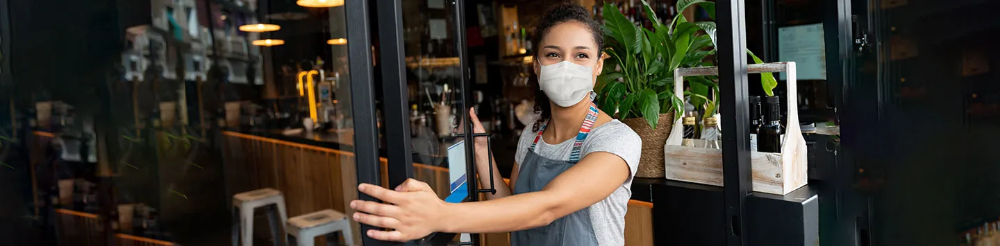 A cafe owner, wearing a mask while opening the doors of their business