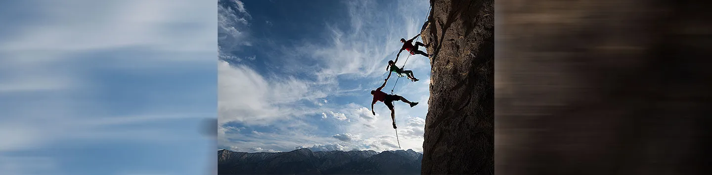 Three rock climbers helping one from falling in a dramatic setting