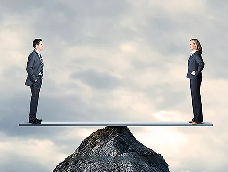 A business man and women balance on a mountaintop.