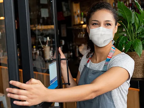 A cafe owner, wearing a mask while opening the doors of their business