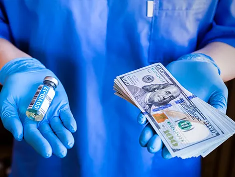 A medical professional holding a Covid-19 vaccine in one hand and 100 dollar bills in the other