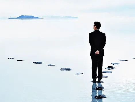 A businessman stands at a fork in the path on a waterway