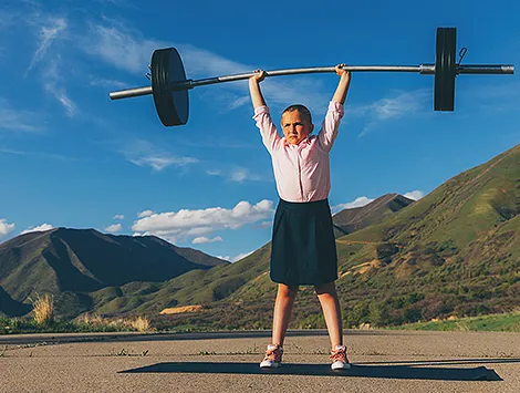 A young girl dressed as a businesswoman is lifting weights