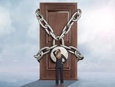 A businesswoman stands in front of a door with a giant padlock on it.