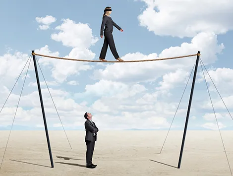 A man watches as a woman crosses a tightrope blindfolded